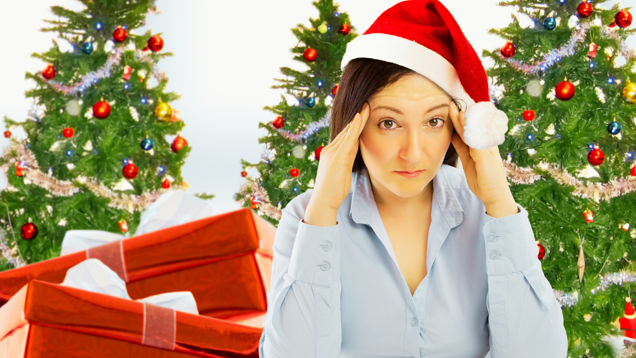 A stressed woman wearing a Santa hat holds her head in frustration while standing in front of brightly decorated Christmas trees and large wrapped presents. Her expression reflects holiday overwhelm, highlighting the emotional and mental health challenges many people face during the holidays. The festive background contrasts with her stress, symbolizing how seasonal pressure, expectations, and emotional strain can affect mental well-being during the holiday season.