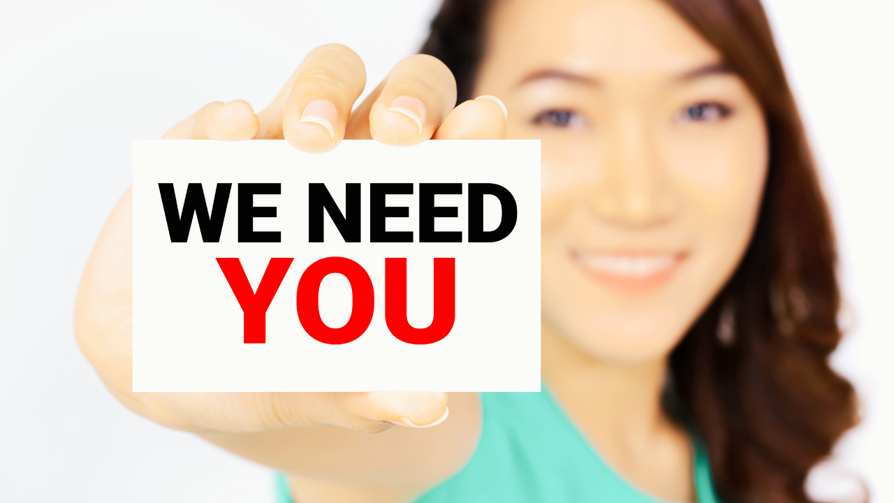 Business professional holding a sign that says “We Need You,” symbolizing employee value, belonging, and engagement within corporate wellness programs. Conceptual image representing how corporate wellness programs support healthier workplace cultures, improve employee wellbeing, strengthen retention, and help organizations build more connected, supported, and high-performing teams.