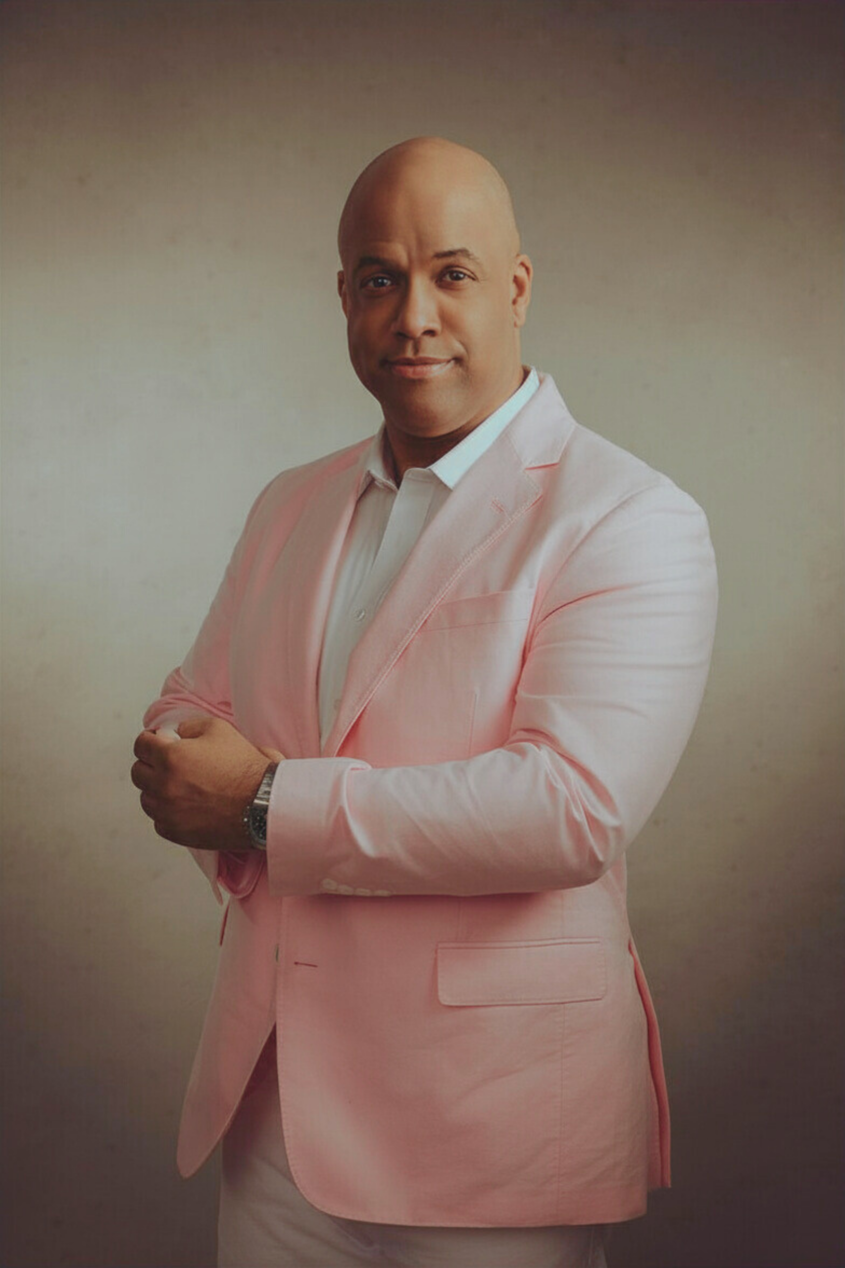 Healthcare conference speaker Mike Veny poses confidently in a light pink blazer and white shirt for professional mental health, workplace wellness, and healthcare event promotion.